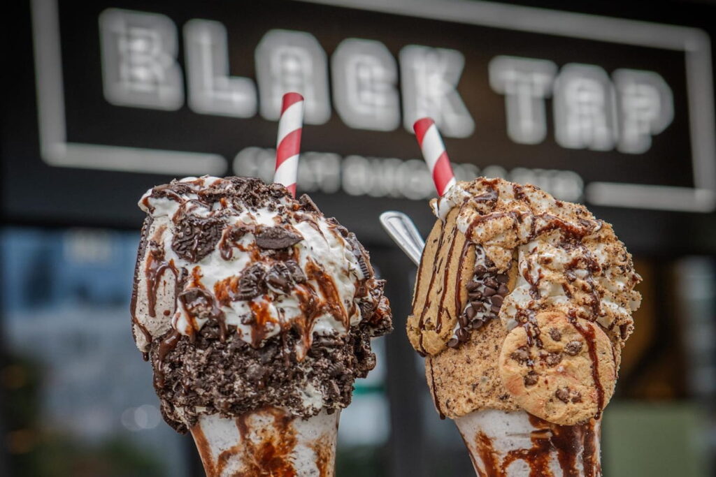 Closeup shot of elaborate milkshakes covered in crushed cookies outside Black Tap Craft Burgers & Beer