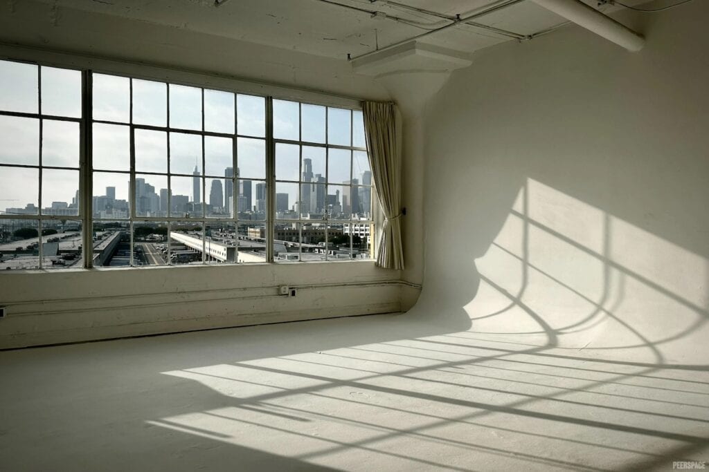 Sunlight filters through large windows onto blank studio space with view of the city
