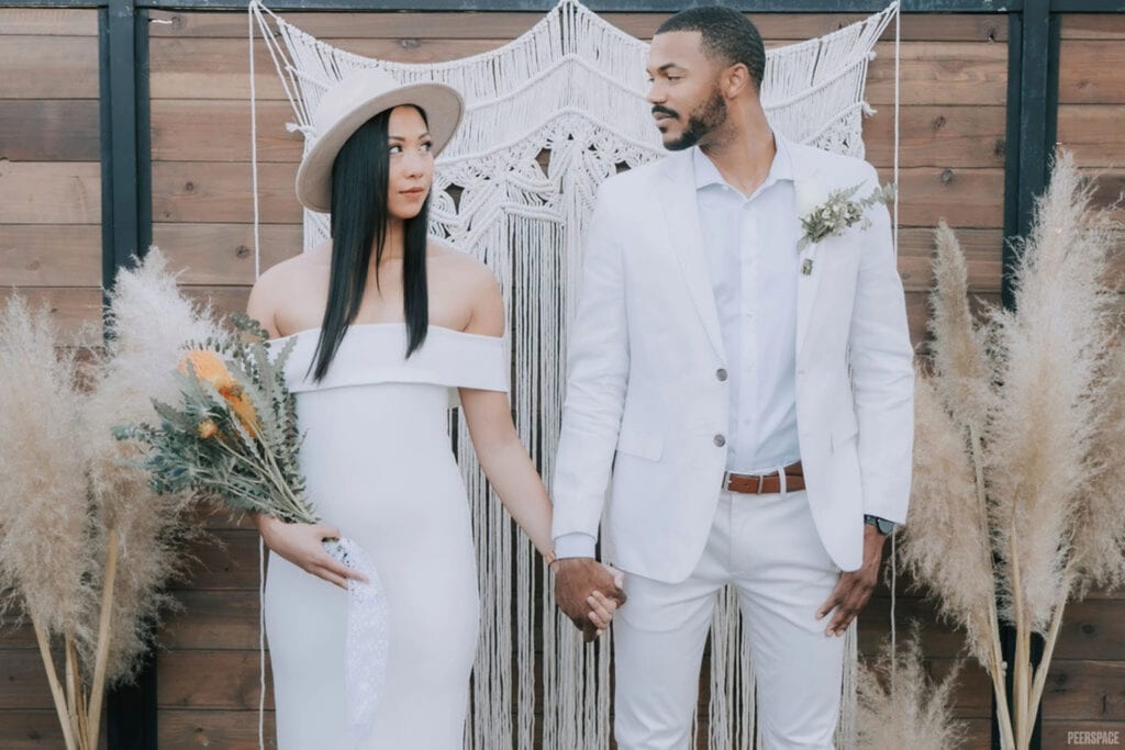 A bohemian-styled bride and groom stand hand-in-hand in front of wooden altar
