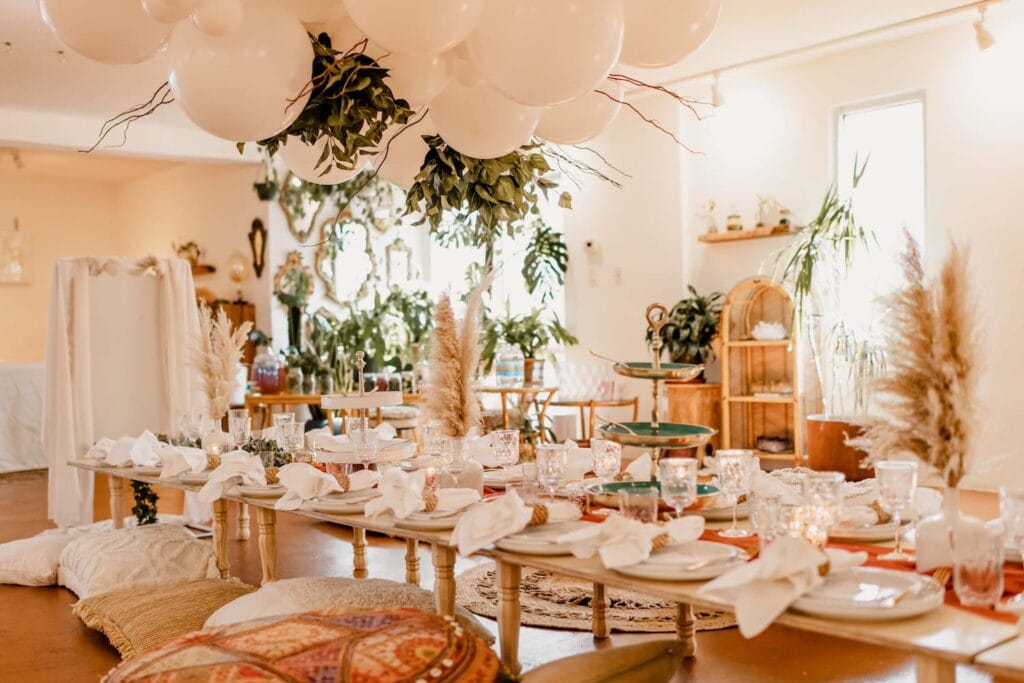 A boho-styled event space with a low-lying table decorated for a meal and surrounded by greenery