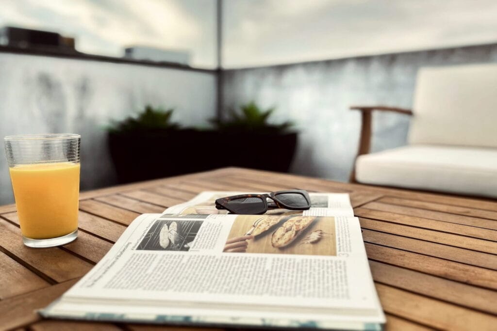 A book and a glass of orange juice sit on an outdoor table on a rooftop in the city.