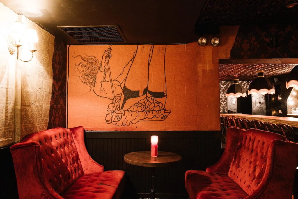 Interior shot of Bordel in Chicago featuring red velvet couches and a drawing of a woman on a wooden swing