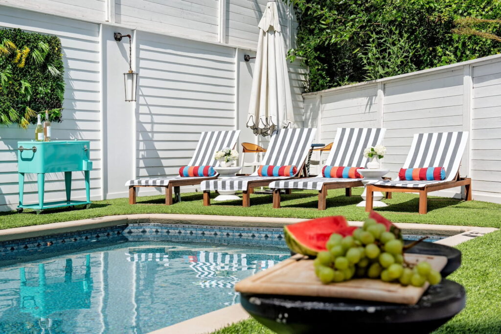 Sunny backyard with pool, striped lounge chairs, an aqua cooler and a platter of fruit in the foreground