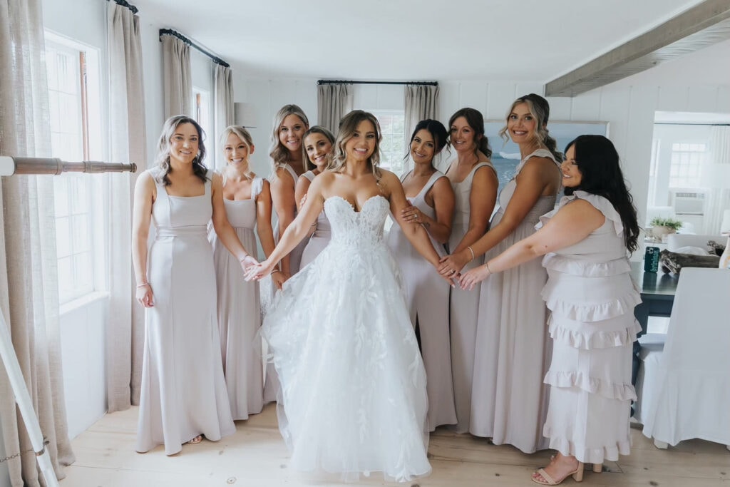 A bride poses with her bridal party in a brightly lit home as they all smile at the camera