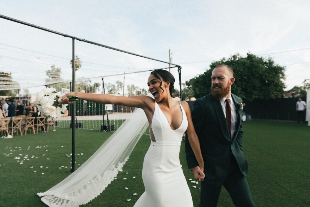 A bride and groom look back at friends and family while smiling widely