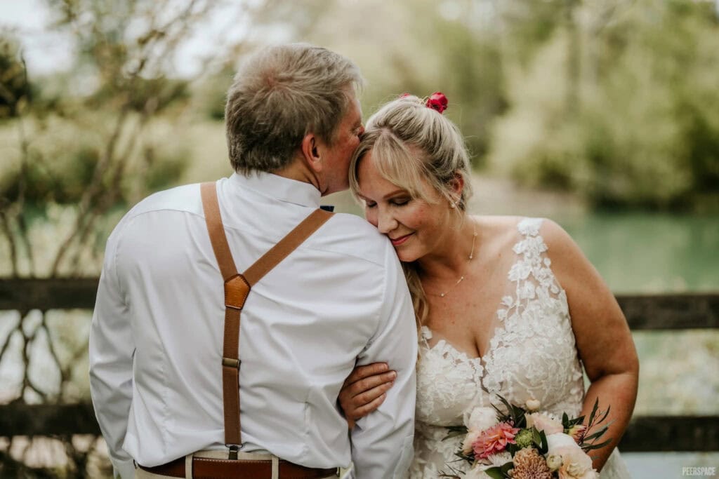 A tender moment of a groom kissing his bride on the forehead at an outside venue