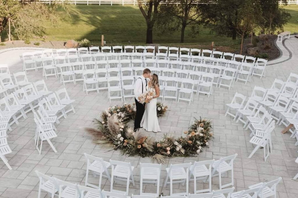 A bride and groom share a kiss on a patio surrounded by ceremony chairs set up in a circle