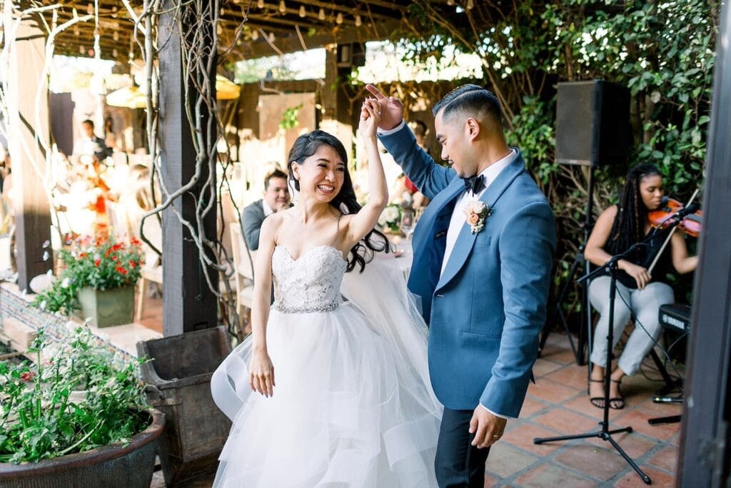 A groom admires his bride as he twirls her on an outdoor patio