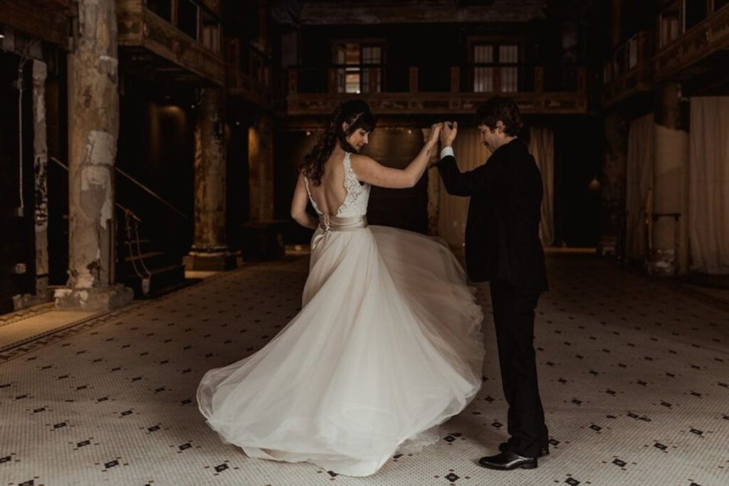 A groom spins his bride in a grand event space with marble columns and tiled flooring