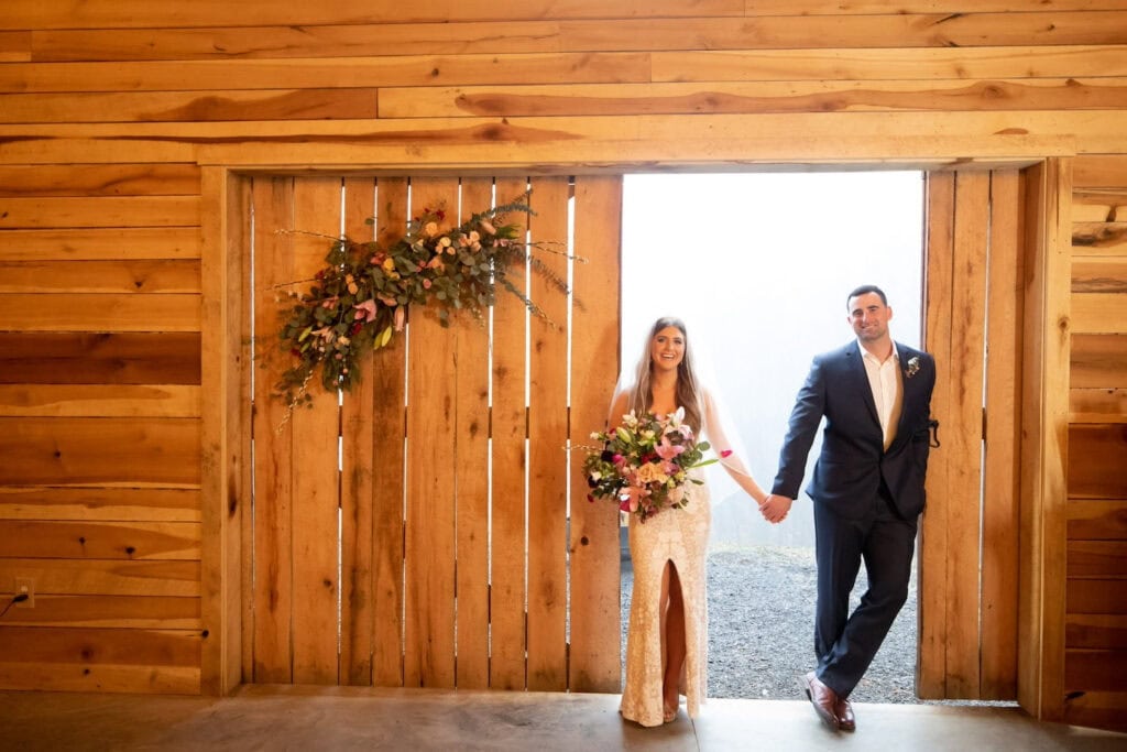 A bride and groom stand in the doorway of a barn