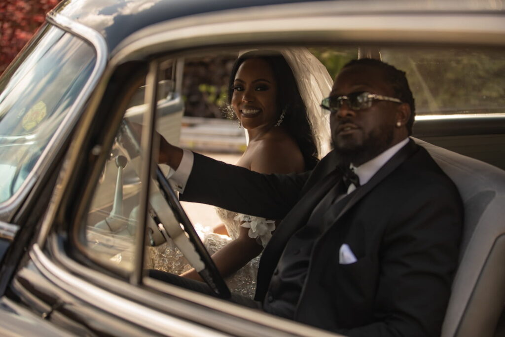 A bride and groom smile at the camera from inside an antique car