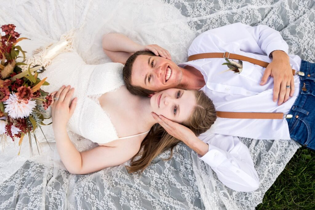 A bride and groom lay on the ground, head to head