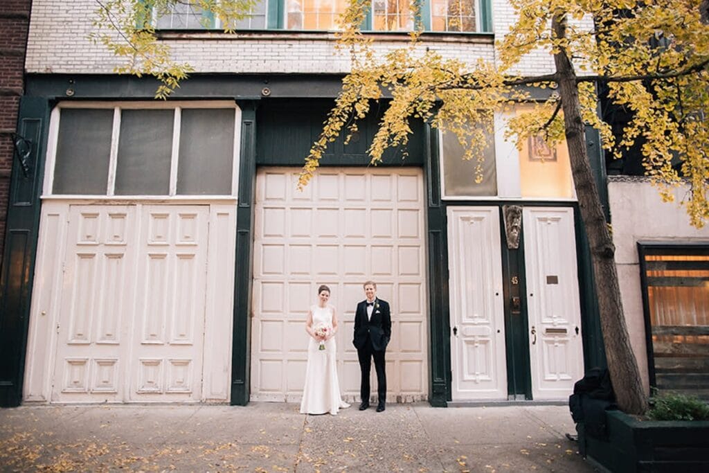A bride and groom stand side by side outside tall doorways on a city street