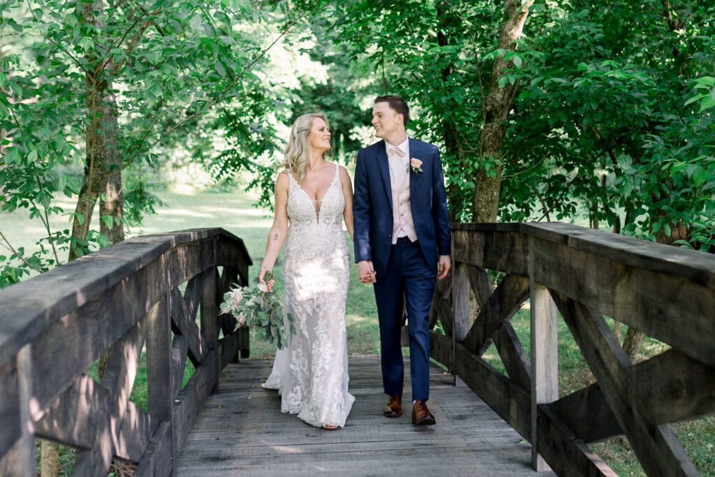 A bride and groom walk hand-in-hand across a wood bridge