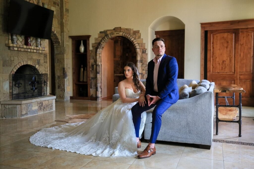 A bride and groom pose for a formal portrait inside a mansion by a fireplace