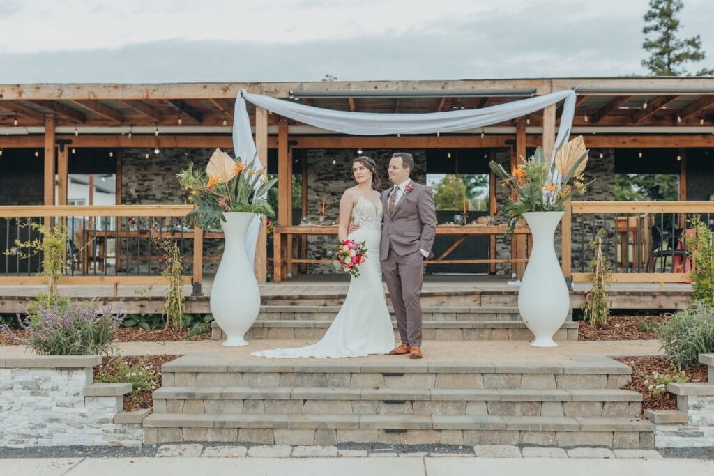 A bride and groom pose on stone steps outside of a rustic stable turned wedding venue