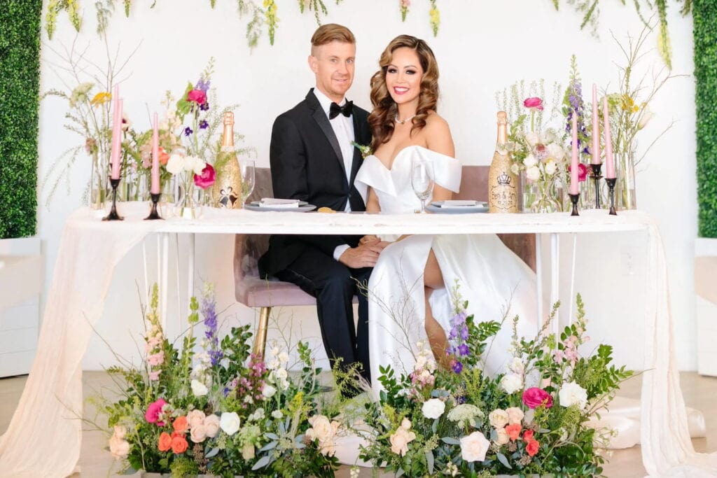A bride and groom pose at a sweetheart table decorated with wild flowers