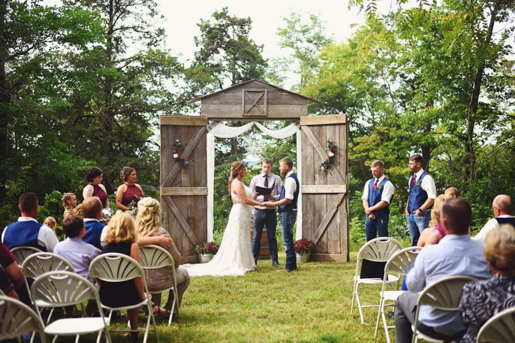 A bride and groom exchange vows in an outdoor ceremony with an altar constructed of barn doors