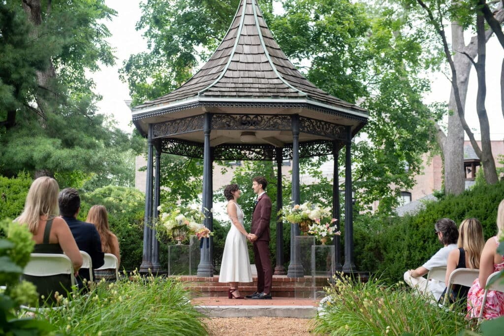 A bride and groom exchange vows next to a gazebo in a park