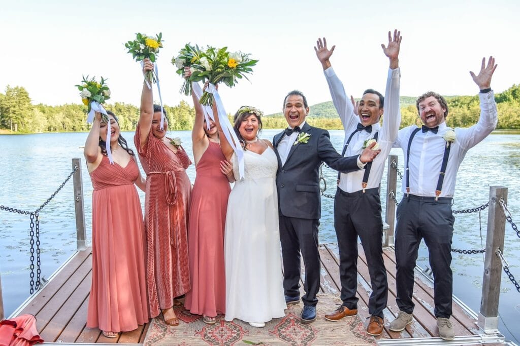 A bride and groom celebrate with their wedding party on a dock by a lake