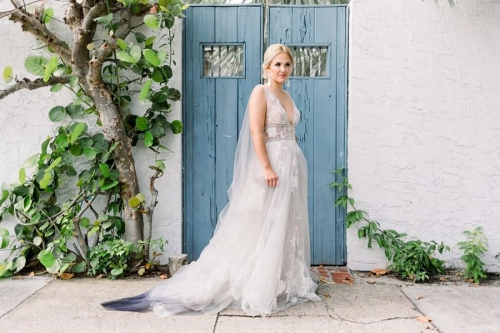 A bride stands outside in front of a white stucco home with a blue wooden door