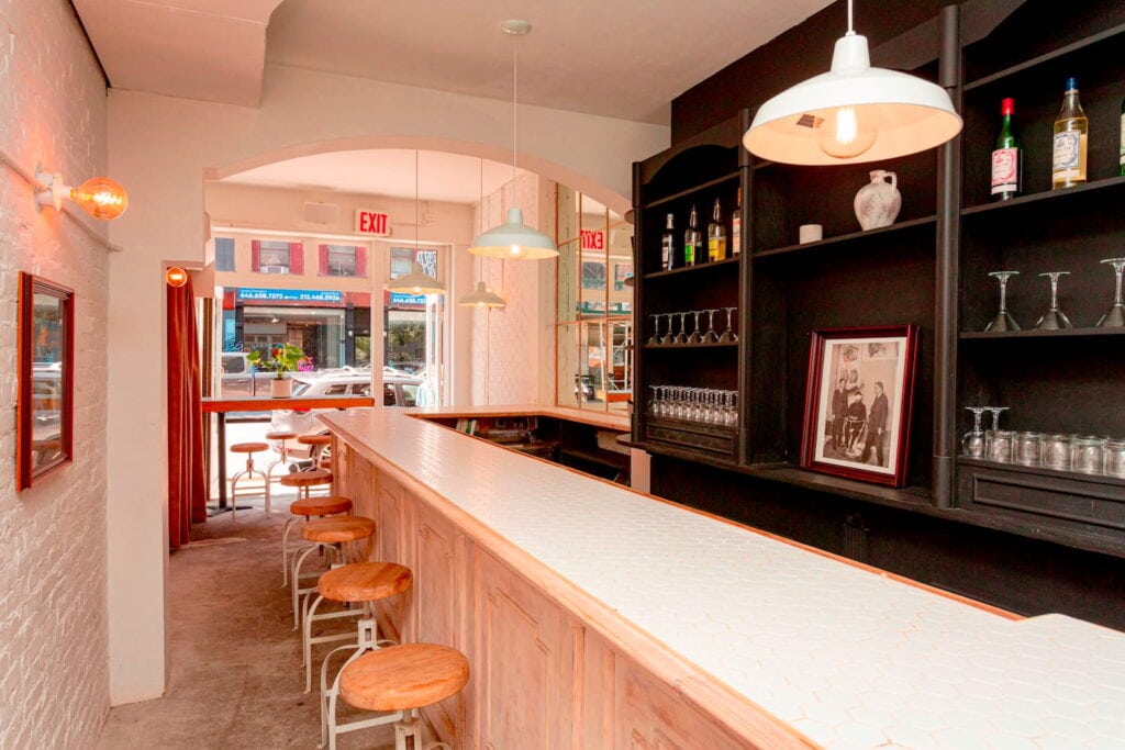 Bright, cheery New York City bar space with open window at the front, light brick walls and dark back bar