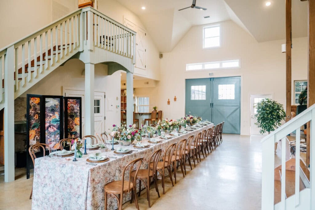 An intimate and sweet reception table is set up in a bright, finished barn with giant blue barn doors and loads of sunlight