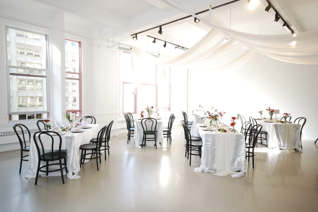 Bright loft space with large windows set up for a simple reception with small tables dressed in white linens