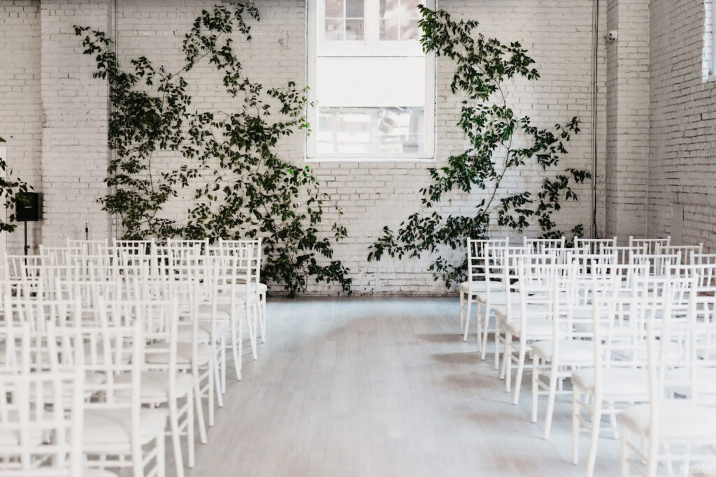 Painted white brick and simple greenery create an altar in a brightly-lit, all white reception space