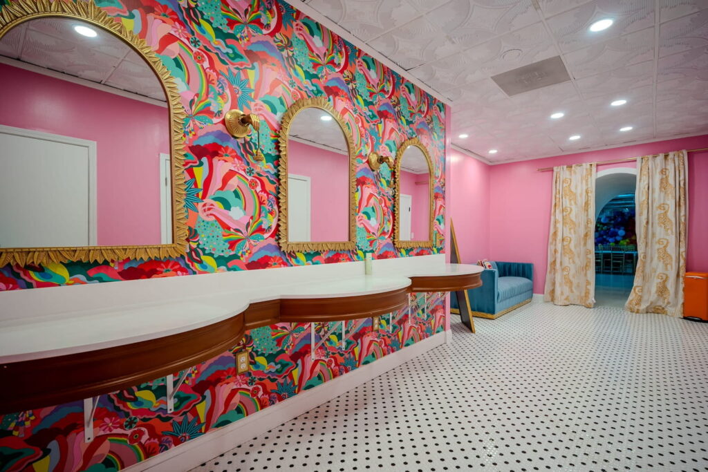 Three separate makeup stations are set against a brightly-wallpapered wall in a bright pink room with aqua accents