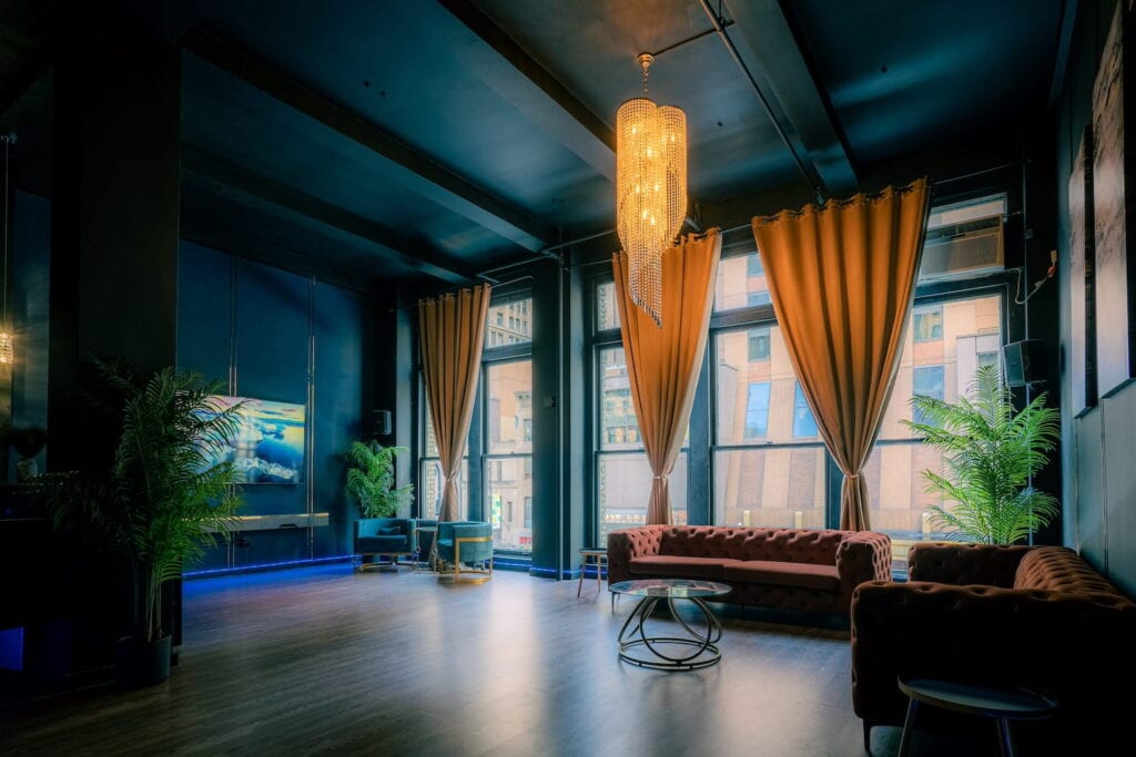 A moody lounge space with large windows, velvet furniture, deep blue walls and gold accents