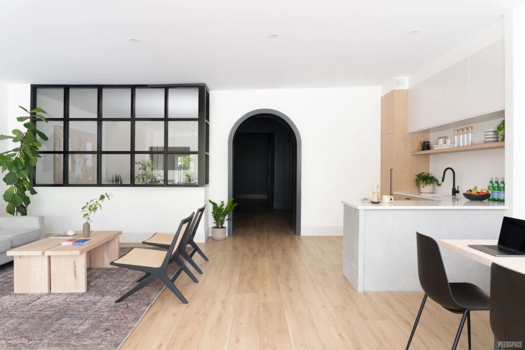 A small office space with contrasting light and black furniture, decorated with plants and a glass-enclosed office area