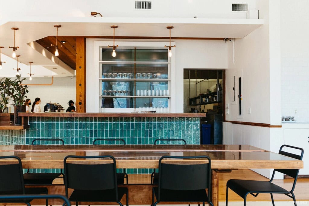 Cafeteria-style gathering space with kitchen area, green and wood accents and industrial lighting