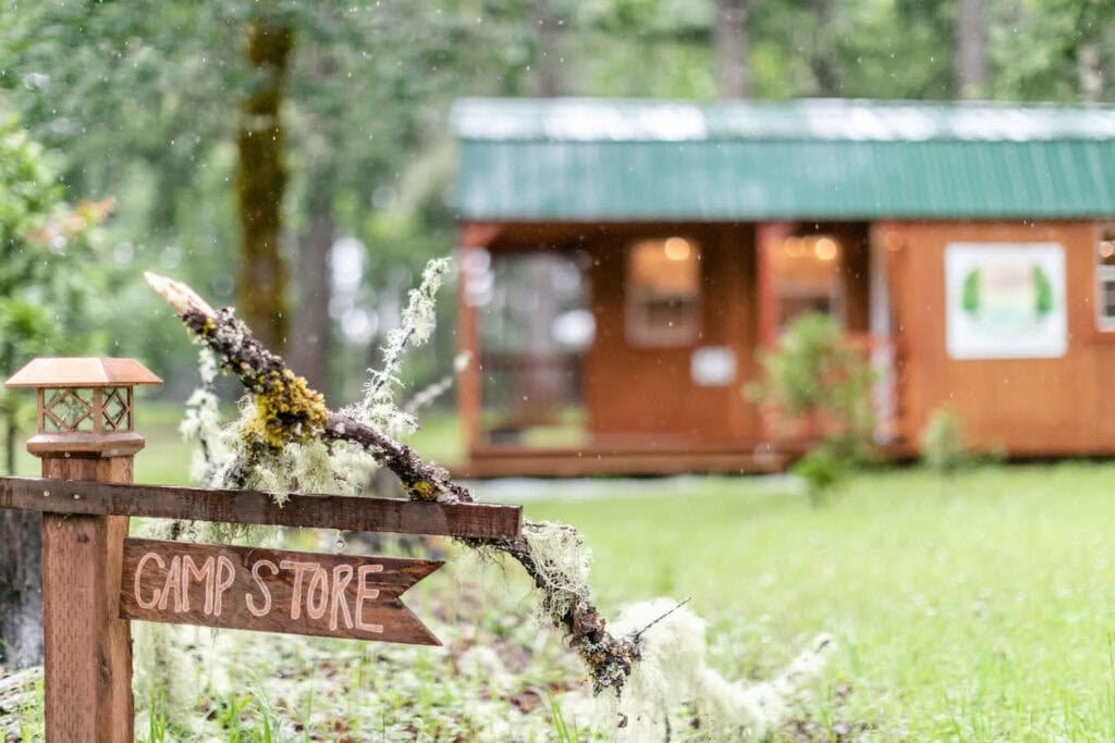 Close up of a sign reading "Camp Store" with a small wooden cabin in the background