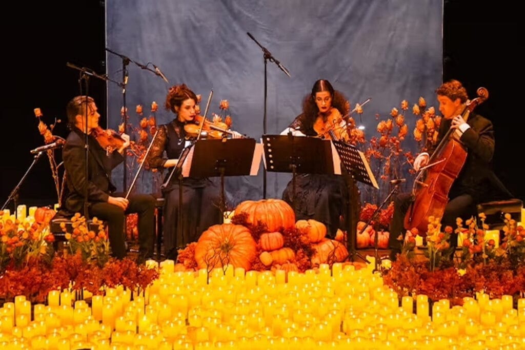 A string quartet performs on a stage full of pumpkin, candles, and other fall decor