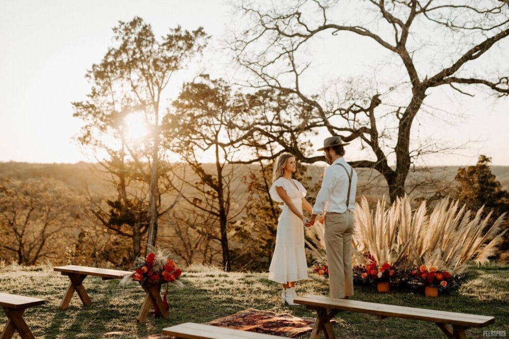 A casually-dressed bride and groom stand at an outdoor altar at sunset