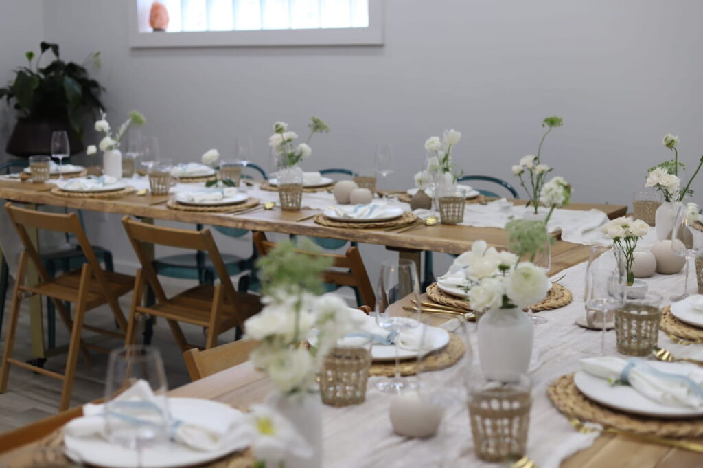 Long wooden tables decorated with white and green flowers and natural accents set up for a meal