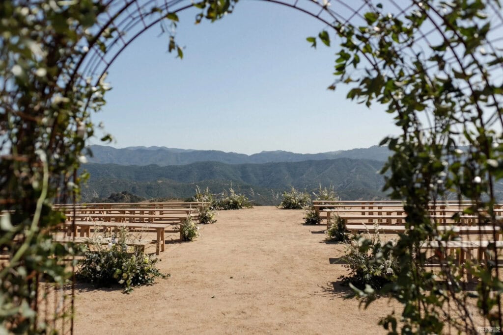Long benches are set up at an outdoor ceremony site with a mountainous backdrop