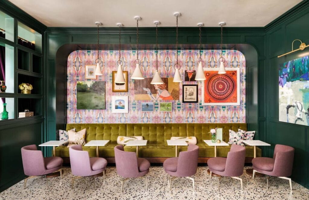 Lush bar space with pink and green velvet seating and a wall of art