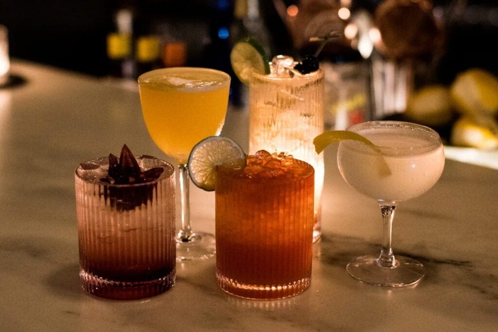 Close up of a selection of cocktails sitting on a bar backlit by a candle