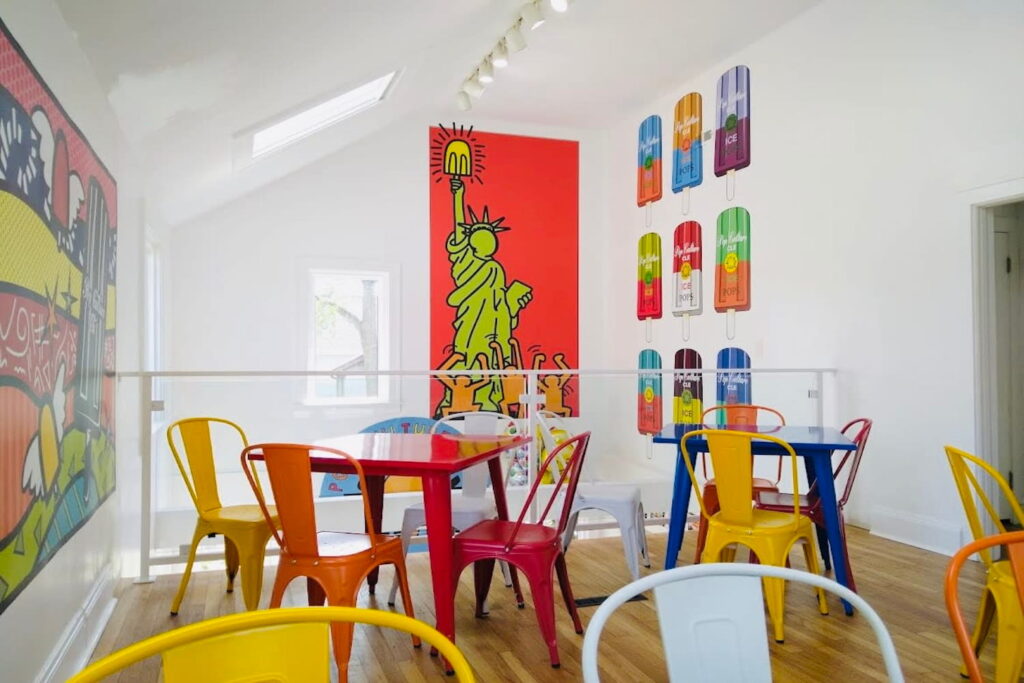 Bright art hangs on white walls in a cheery event space with colorful tables and chairs