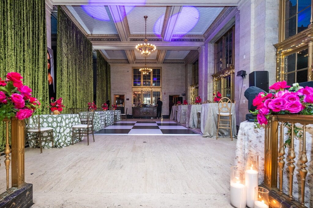 A converted bank space decorated with green velvet drapery, gold accents and a black and white checkered dance floor