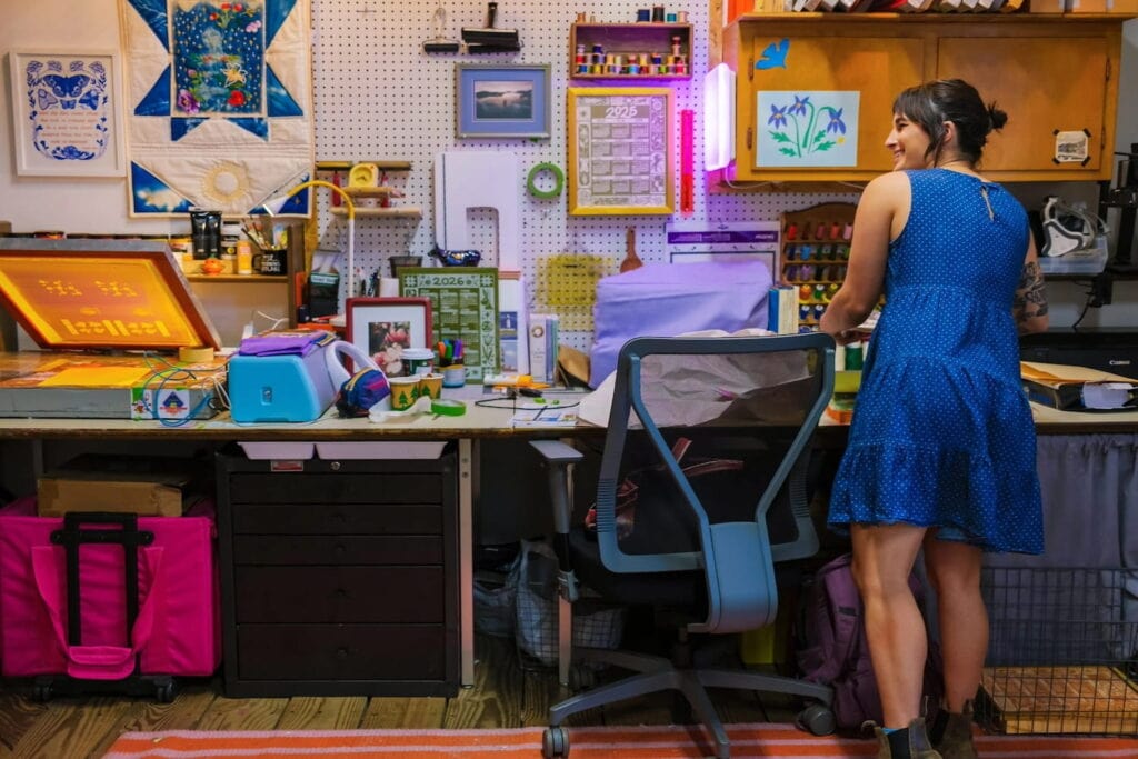 A woman stands by a desk filled with art supplies
