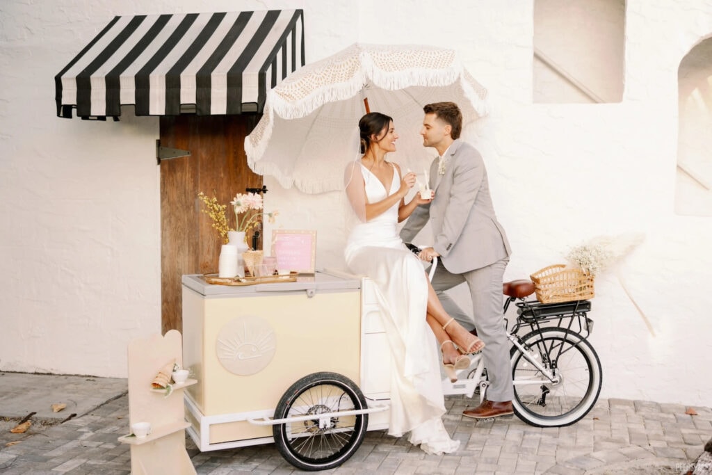 A couple poses under the umbrella of a beverage cart