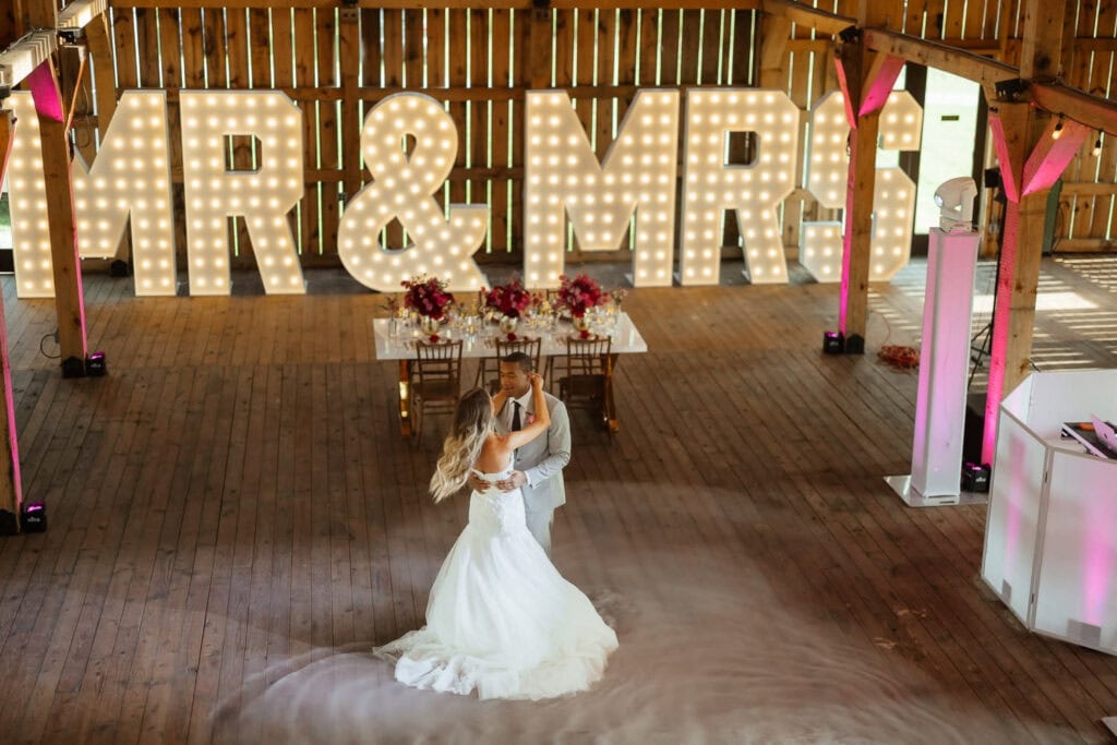 A bride and groom share a dance in front of a giant. light up Mr. & Mrs. sign