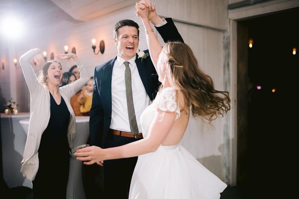 A groom gleefully spins his bride on the dance floor as guests celebrate behind them