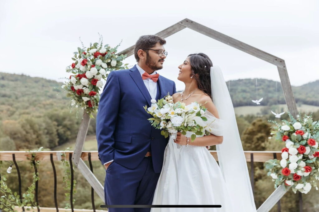 A bride and groom look lovingly at each other while standing by a wooden altar outside with tree-lined hills in the distance