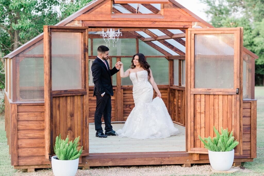 A bride and groom dance under a chandelier in a small wooden greenhouse
