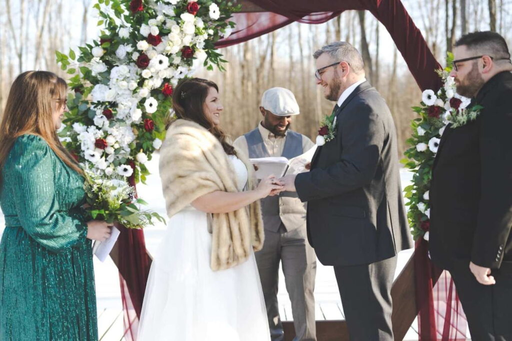 A bride and groom exchange vows outside in the winter by an altar decorated in white and red flowers