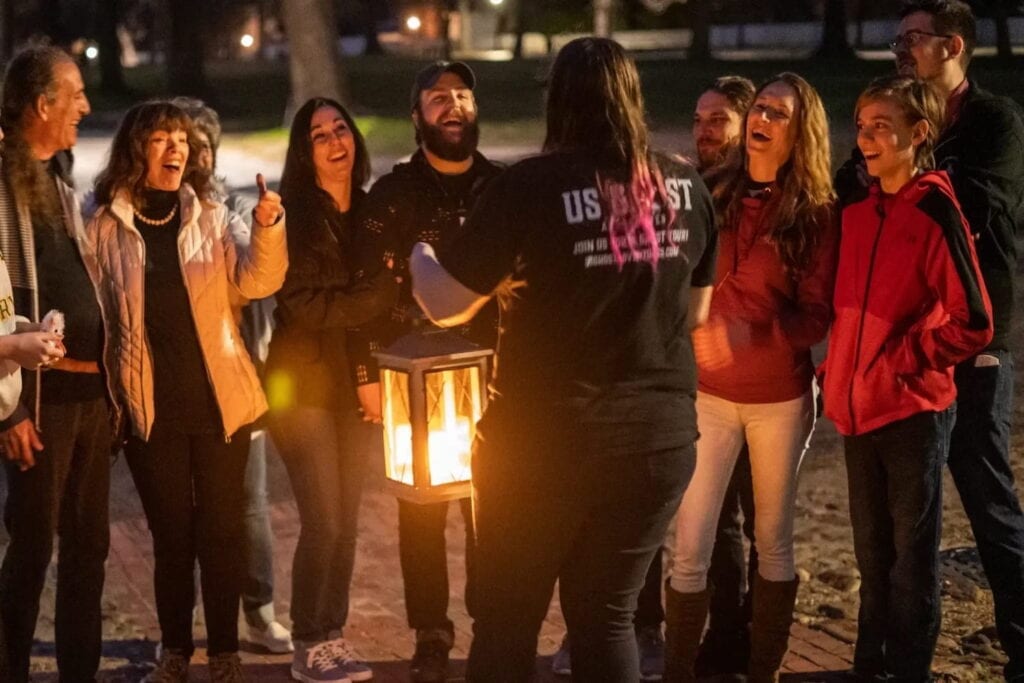A group on a ghost tour smiles at their tour guide who is carrying a lantern